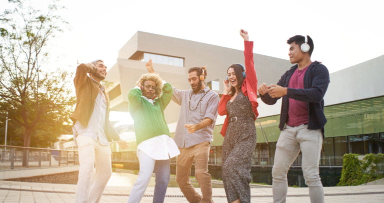 Group of happy people outdoors celebrating and dancing with headphones outdoors.