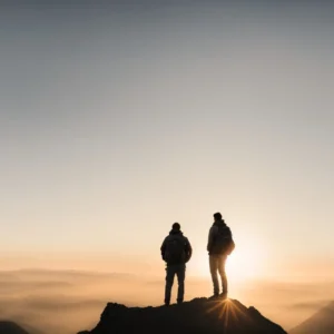 a person standing confidently on the peak of a mountain with a sunrise casting a silhouette in the background.