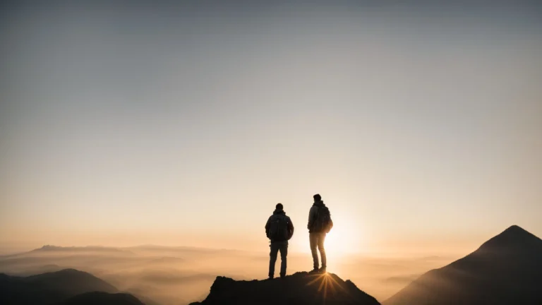 a person standing confidently on the peak of a mountain with a sunrise casting a silhouette in the background.