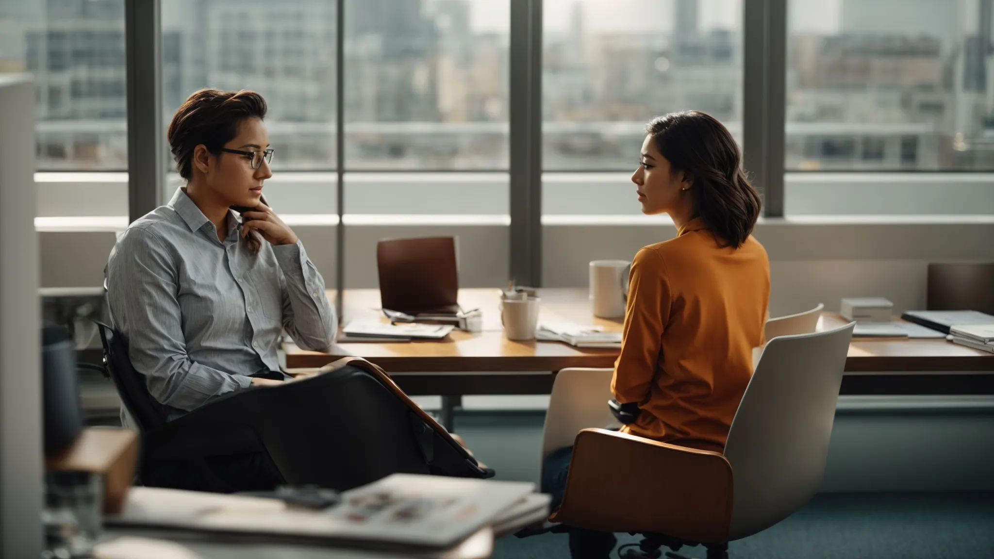 two colleagues are seated across from each other in a bright office, engaged in a focused conversation.