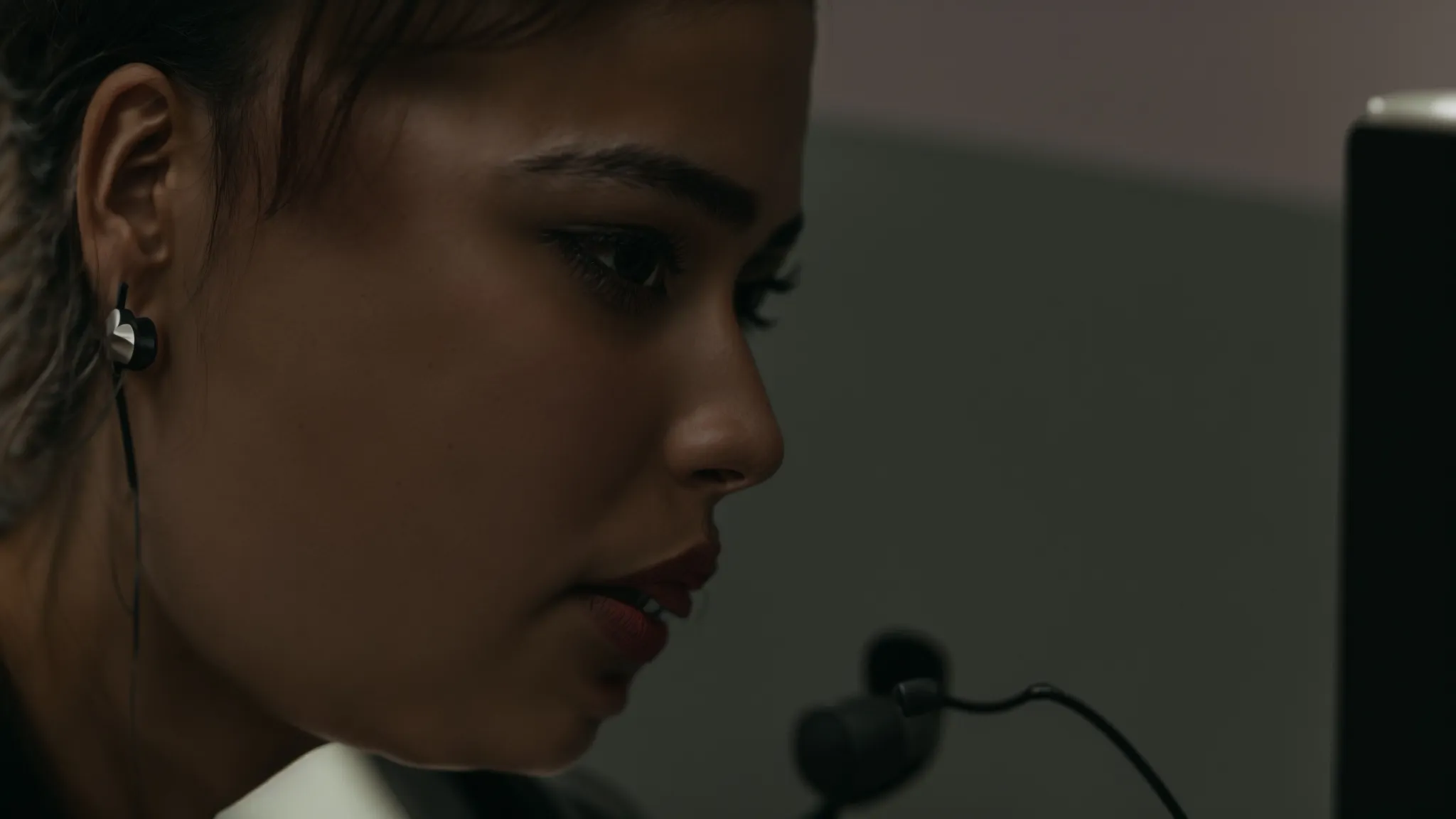a person speaking into a microphone with a computer screen displaying scrolling text in the background.